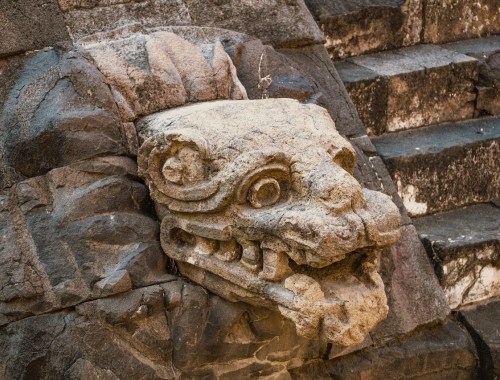 Mexiko Teotihuacán - Aus Stein nachgebildeter Kopf eines Gottes neben den Stufen, die zu einer Pyramide hinaufführen