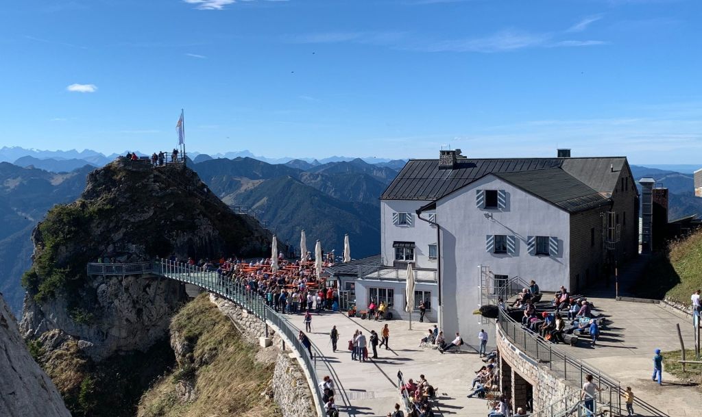 Wendelstein - Blick auf die Wendelsteinhütte und die umliegende Berglandschaft mit vielen Besuchern auf der Terrasse.